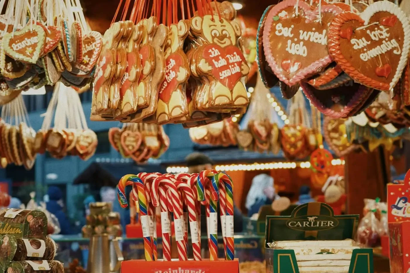 A stall at a Christmas market selling gingerbread hearts, candy canes, and roasted nuts under warm lights.