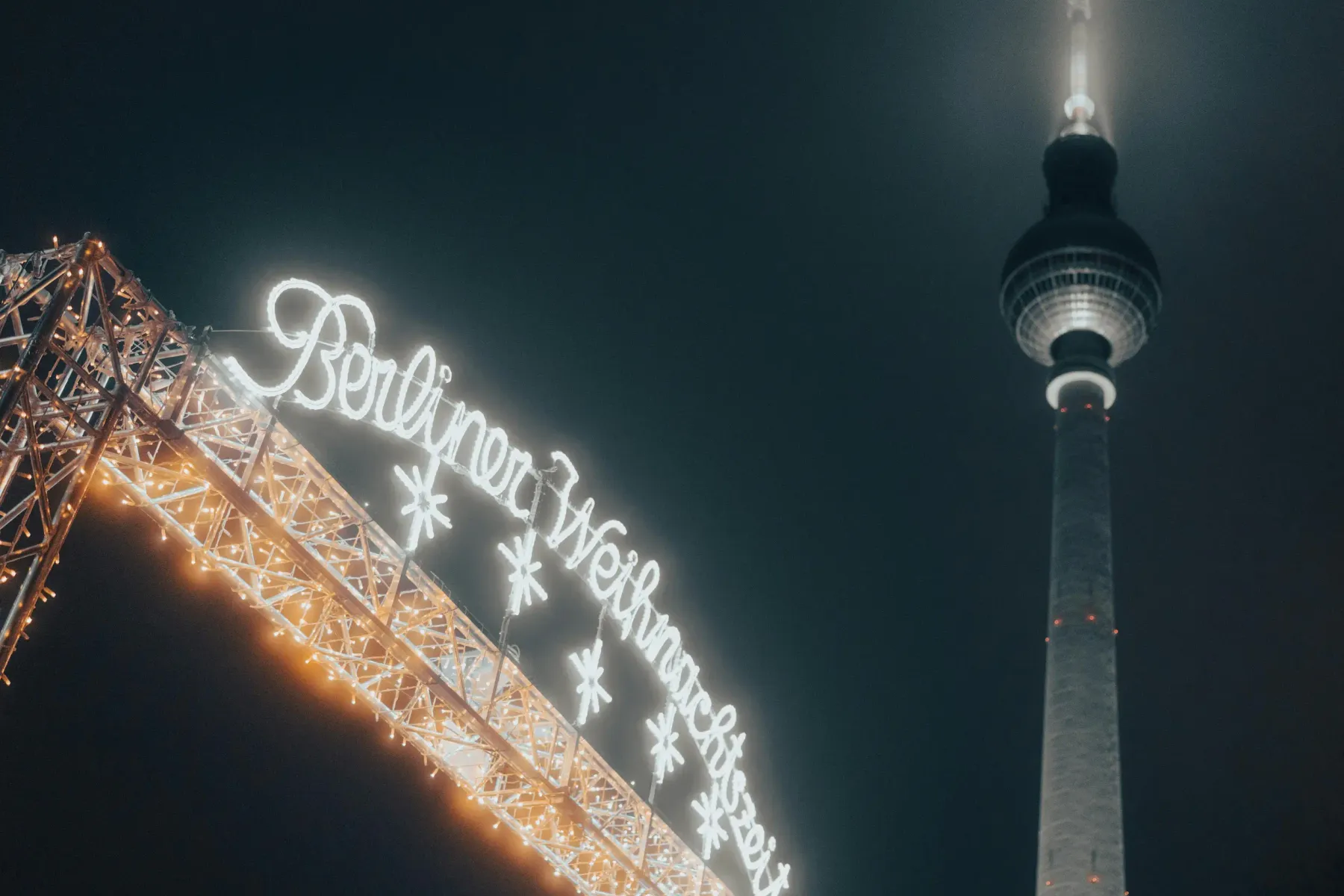 Illuminated 'Berliner Weihnachtszeit' sign and a section of the Berlin TV Tower against a dark night sky.