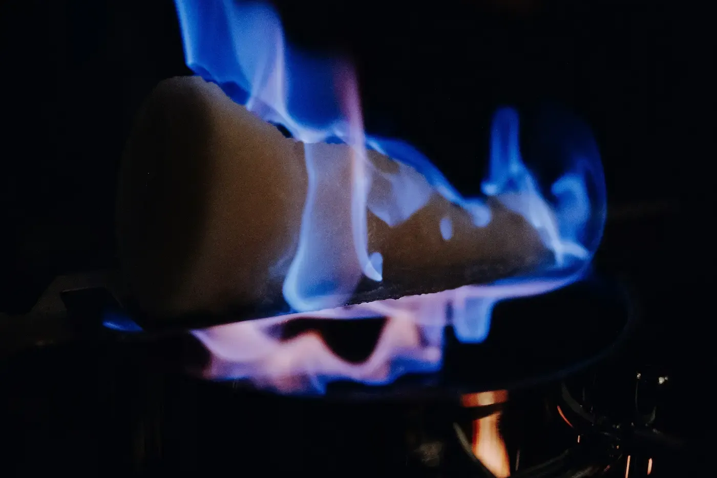 Sugar cone with blue flames burning over a dark pot, illuminating the foreground against a dark background.
