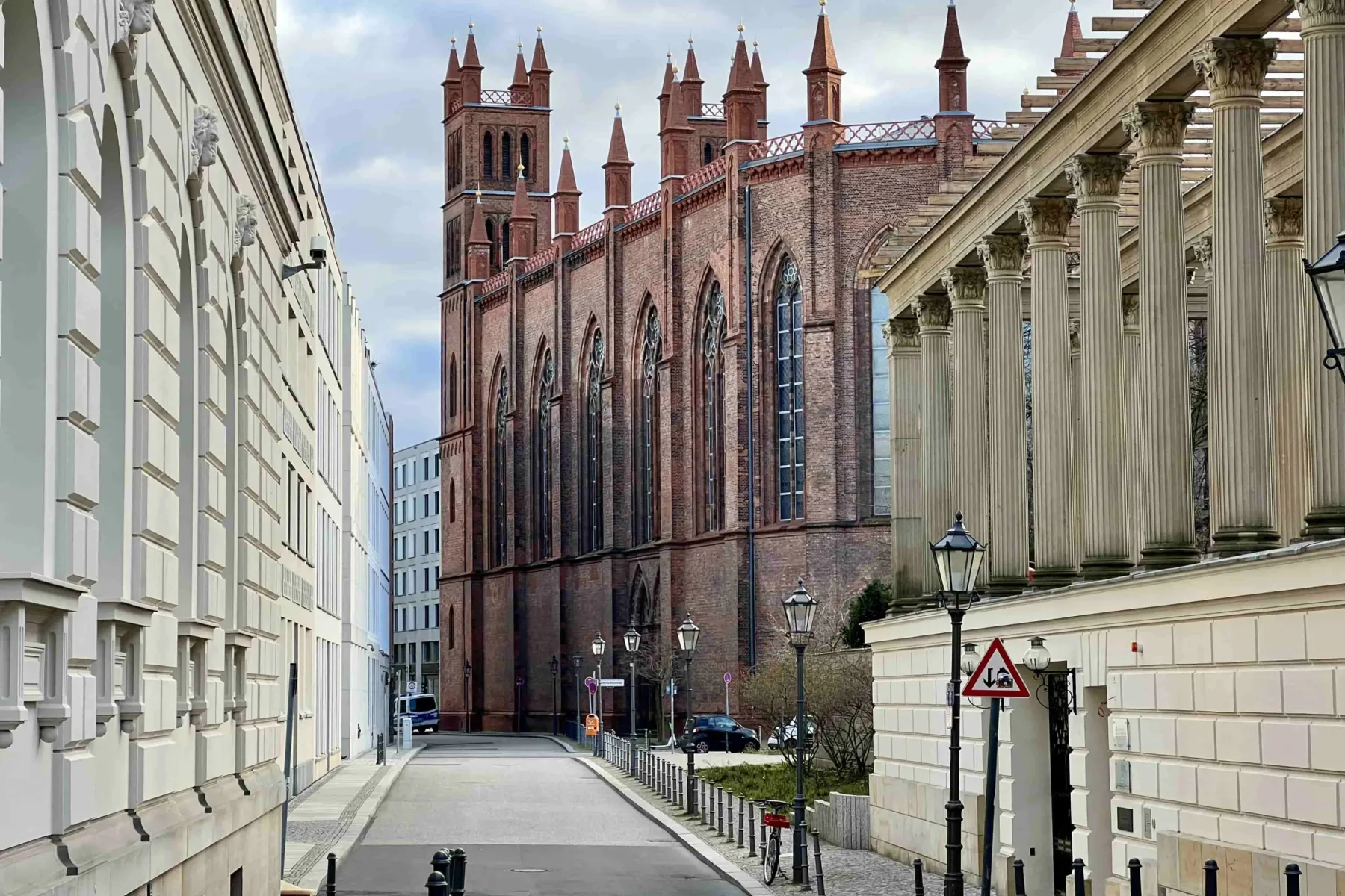 The red-brick Friedrichswerder Church seen from a quiet side street next to a building with a classical colonnade in Berlin.