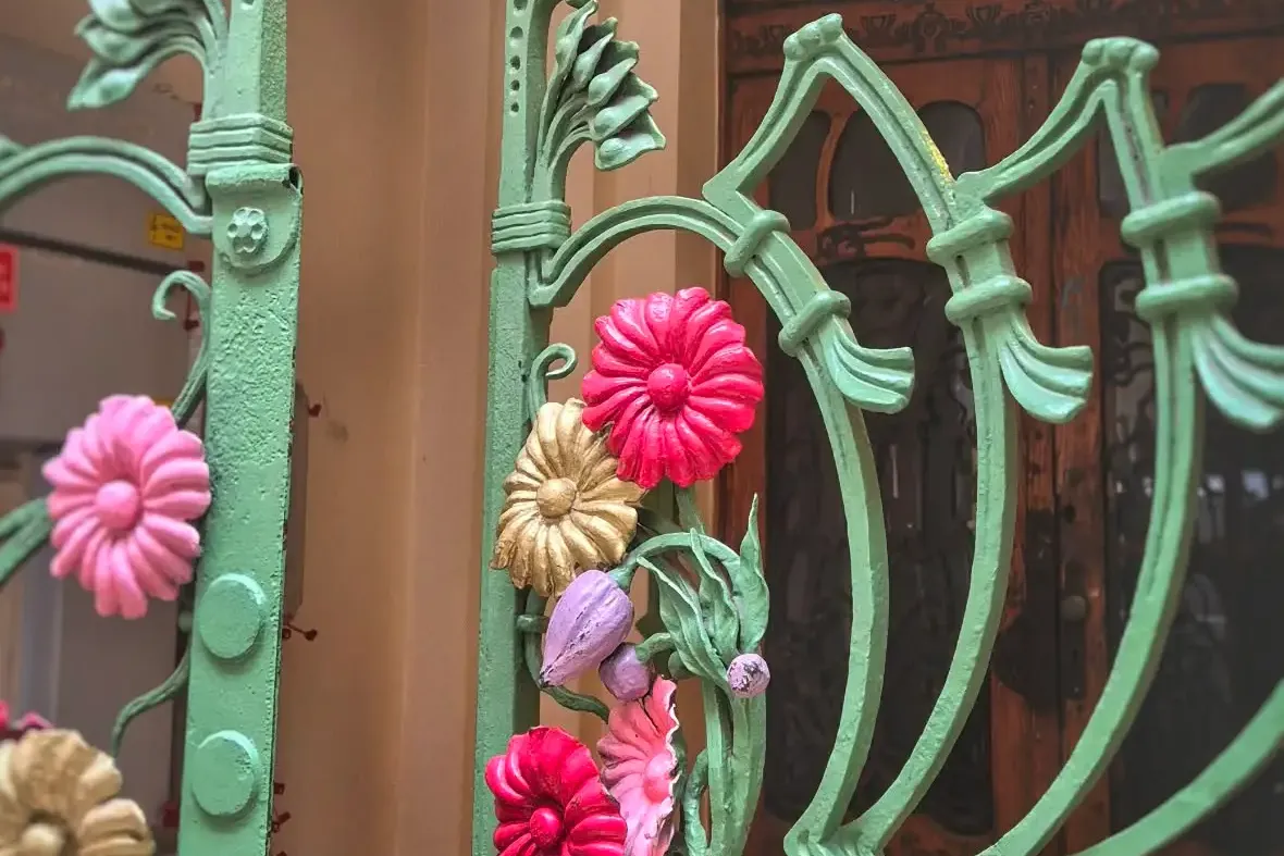 Ornate green Art Nouveau metal gate with colorful pink, gold, and purple floral decorations, in front of an arched wooden ...