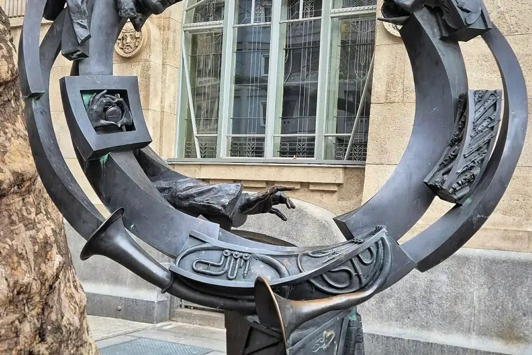 Bronze sculpture in Budapest featuring a man's head, hands, trumpets, piano keys, and abstract forms in a circular design.