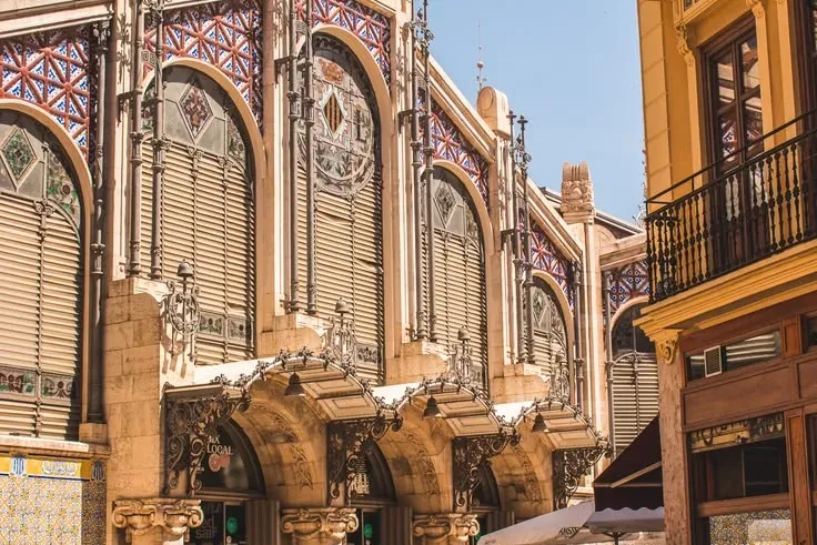 Ornate facade of the Central Market in Valencia, with people walking past on a sunny day.