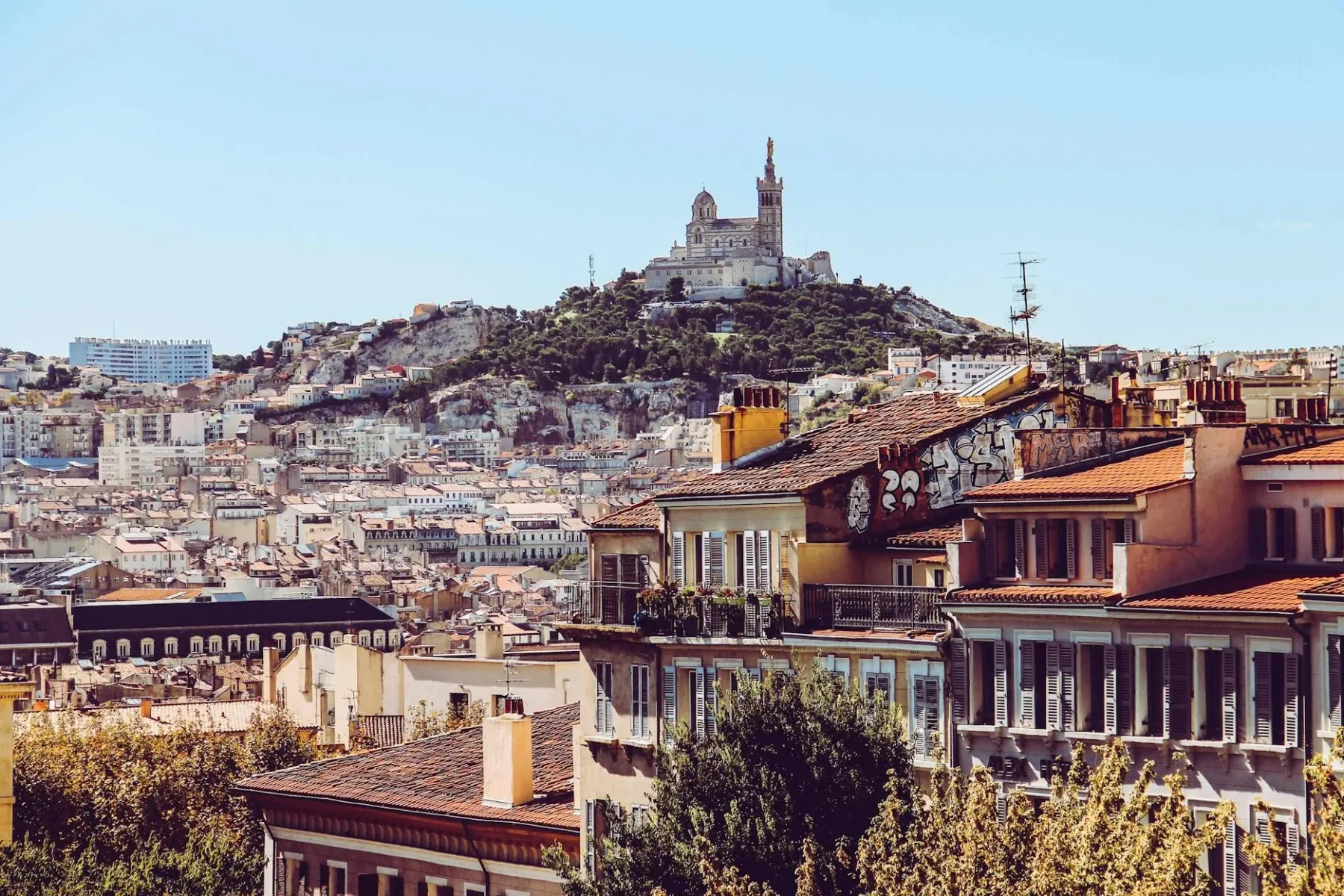 Panoramic view of Marseille with Notre-Dame de la Garde basilica on a hill, surrounded by dense urban buildings with red r...