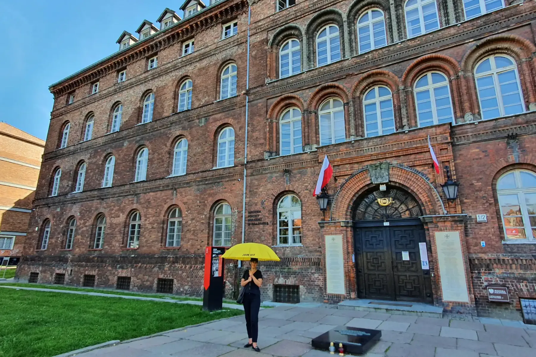 Historic brick building of the Polish Post Office in Gdansk with arched windows, a dark entrance, and Polish flags. A pers...