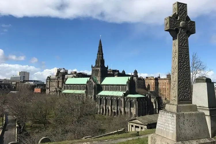 Historic Glasgow Cathedral with green roof and spire, viewed from the Necropolis, showing an ornate Celtic cross in the fo...
