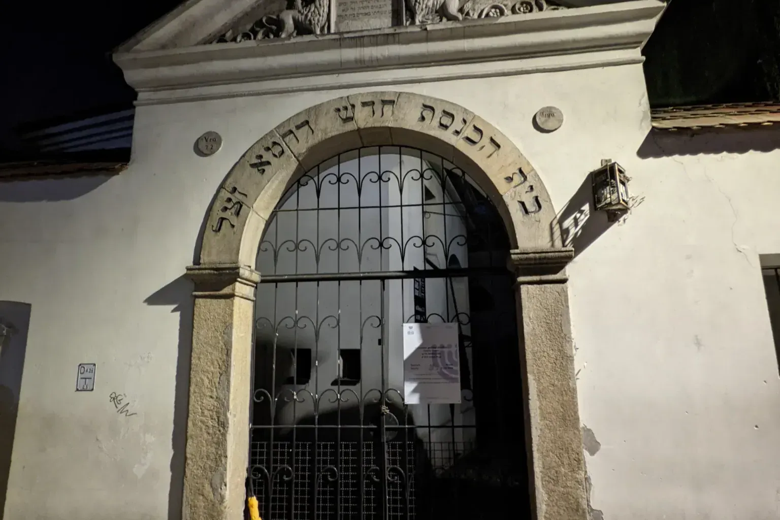 Stone entrance to the Isaak Synagogue in Krakow's Kazimierz district at night, with Hebrew script over an arched gate.
