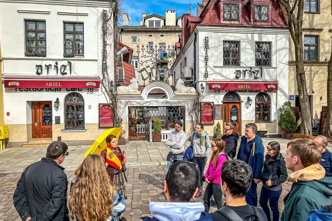 A tour group listens to a guide with a yellow umbrella on Szeroka Street in Krakow's Kazimierz district.