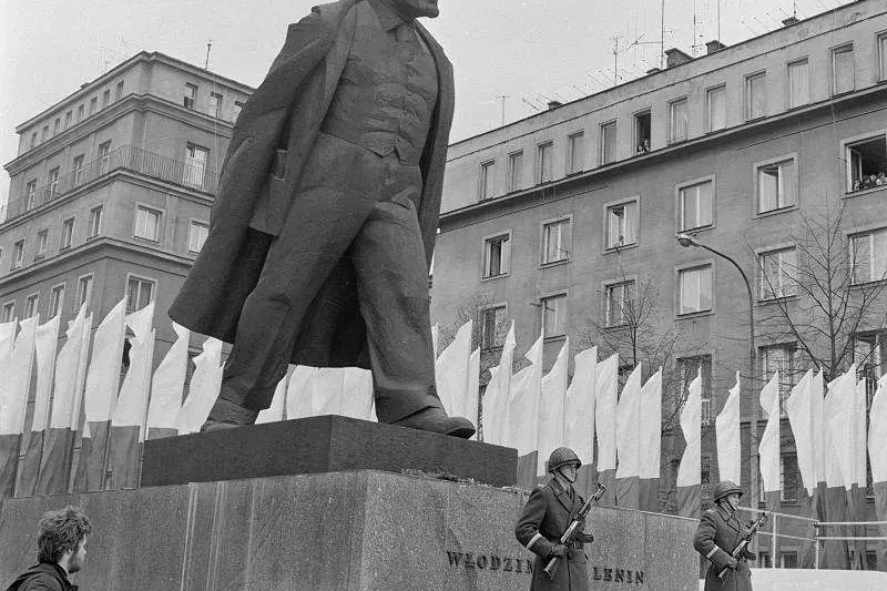 Black and white archive photo of the large Lenin statue in Nowa Huta, with two soldiers standing guard at its base.