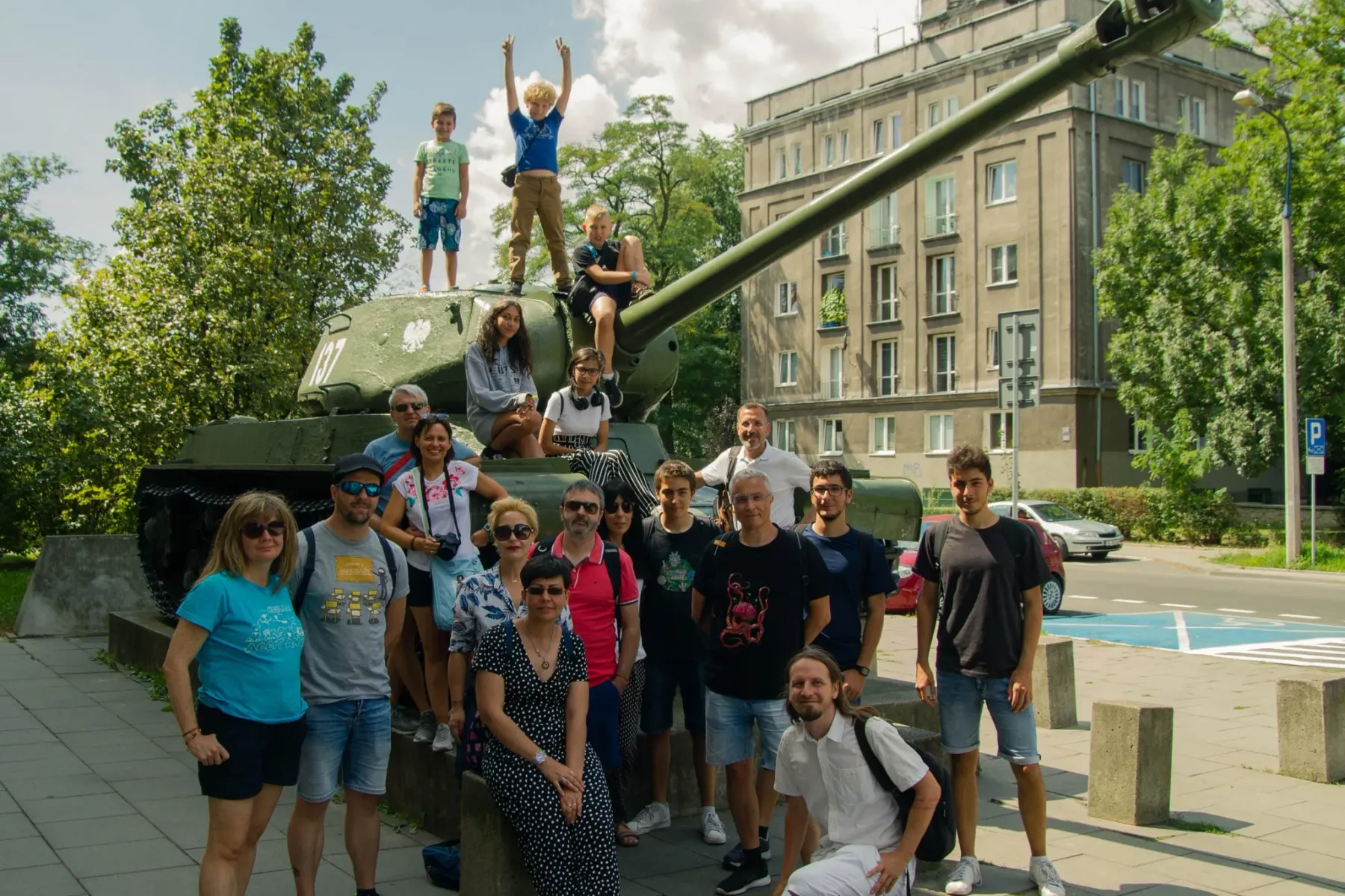 A tour group of adults and children posing for a photo on and around a green IS-2 tank monument in Krakow's Nowa Huta.