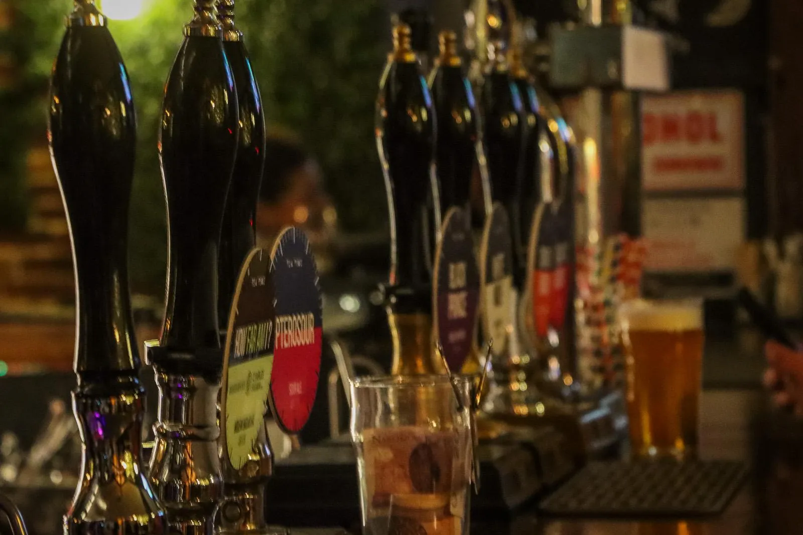 A row of shiny black beer taps on a wooden bar in a dimly lit Krakow pub. A pint glass sits in the background.