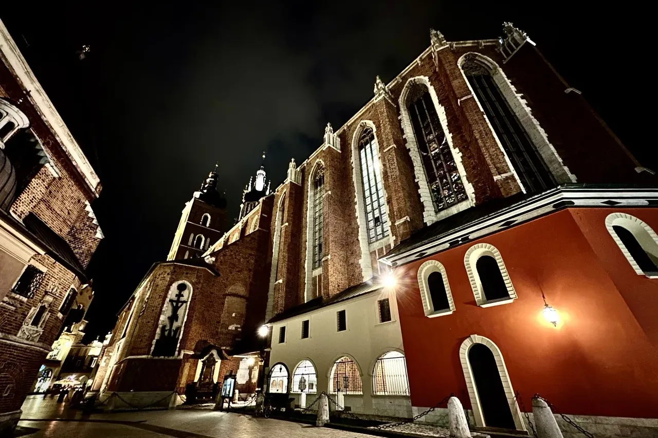 St. Mary's Basilica in Krakow at night, showing its brick facade, gothic windows, and two towers under a dark sky.