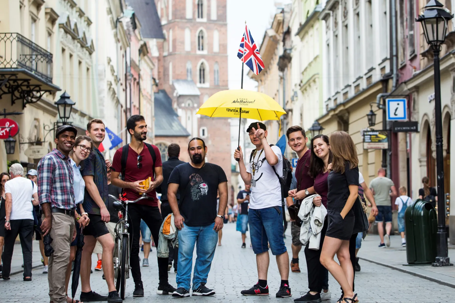 A group of tourists with a guide holding a yellow umbrella on a historic cobblestone street in Krakow's Old Town.