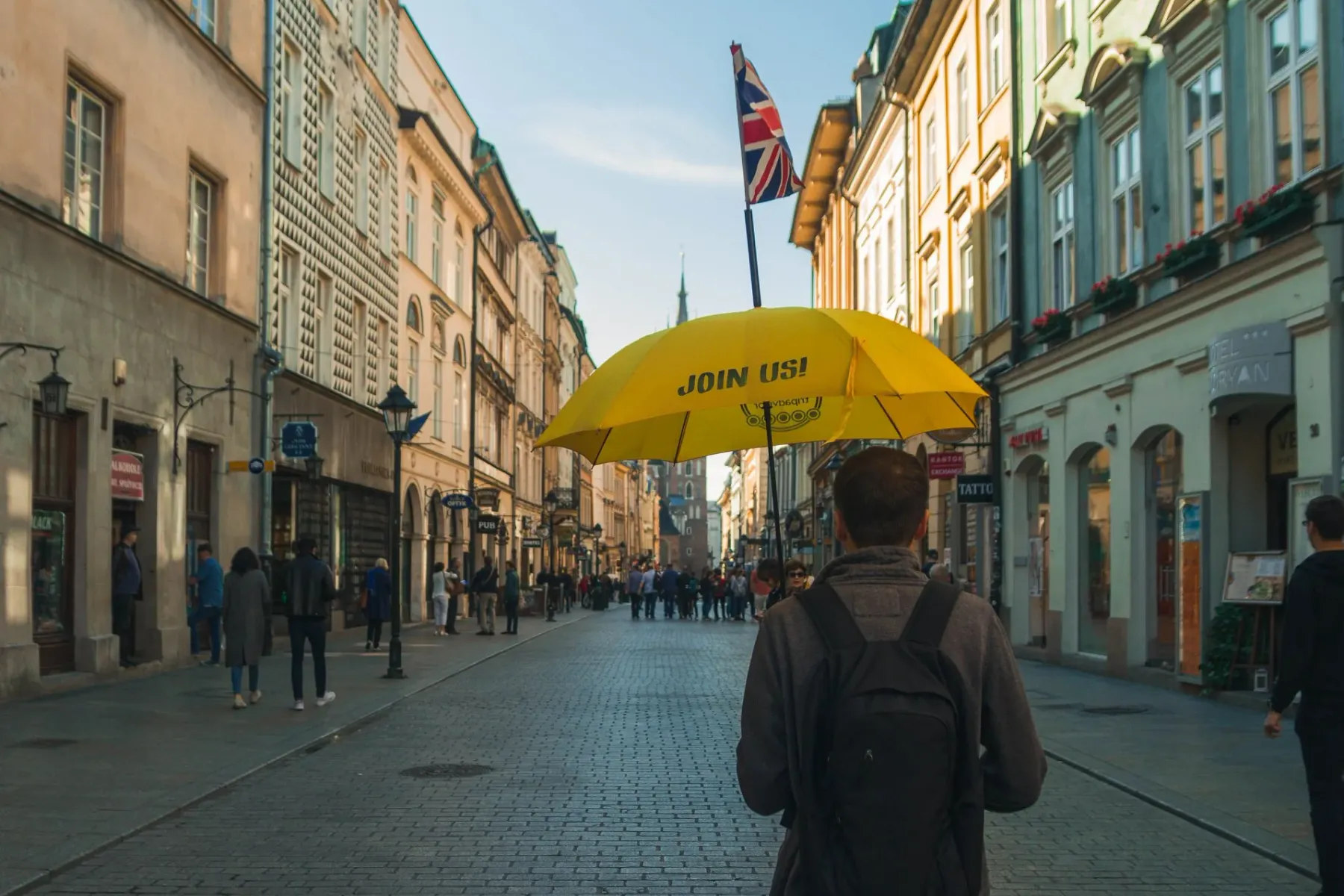 A tour guide holds a yellow umbrella on a historic cobblestone street in Krakow, leading a group toward a church tower.