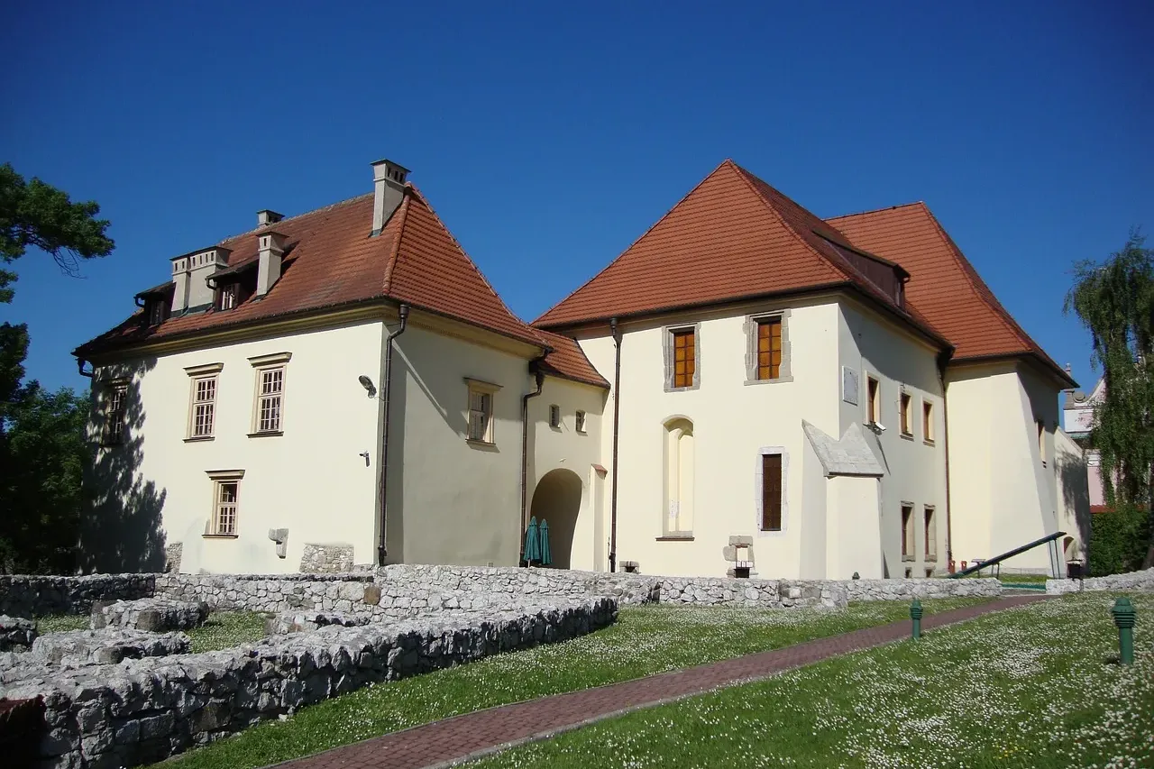 Historic white buildings with red tile roofs at the Wieliczka Salt Mine, with old stone foundations on a lawn in front.