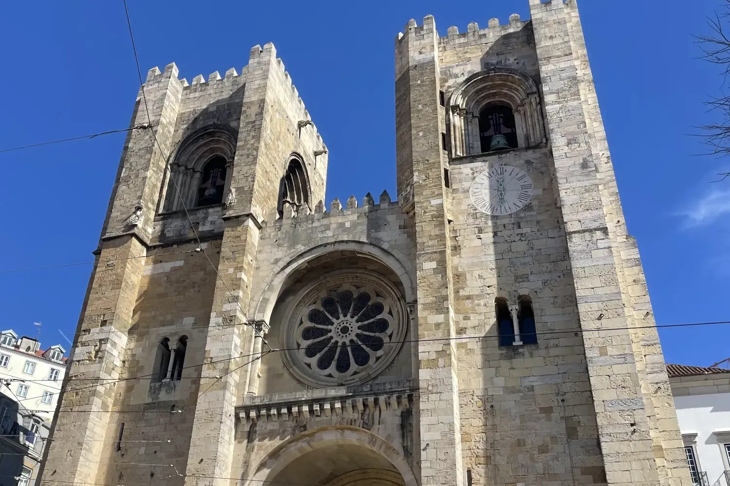 The facade of Lisbon Cathedral (Sé de Lisboa) with two square towers, a central rose window, and an arched entrance under ...