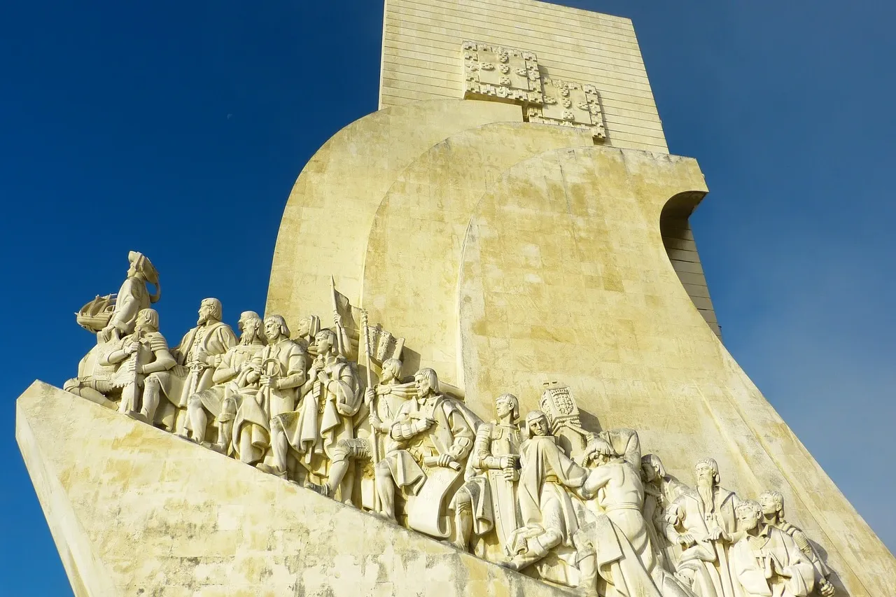 Stone Monument to the Discoveries in Lisbon featuring statues of historical explorers on a ship's prow against a blue sky.