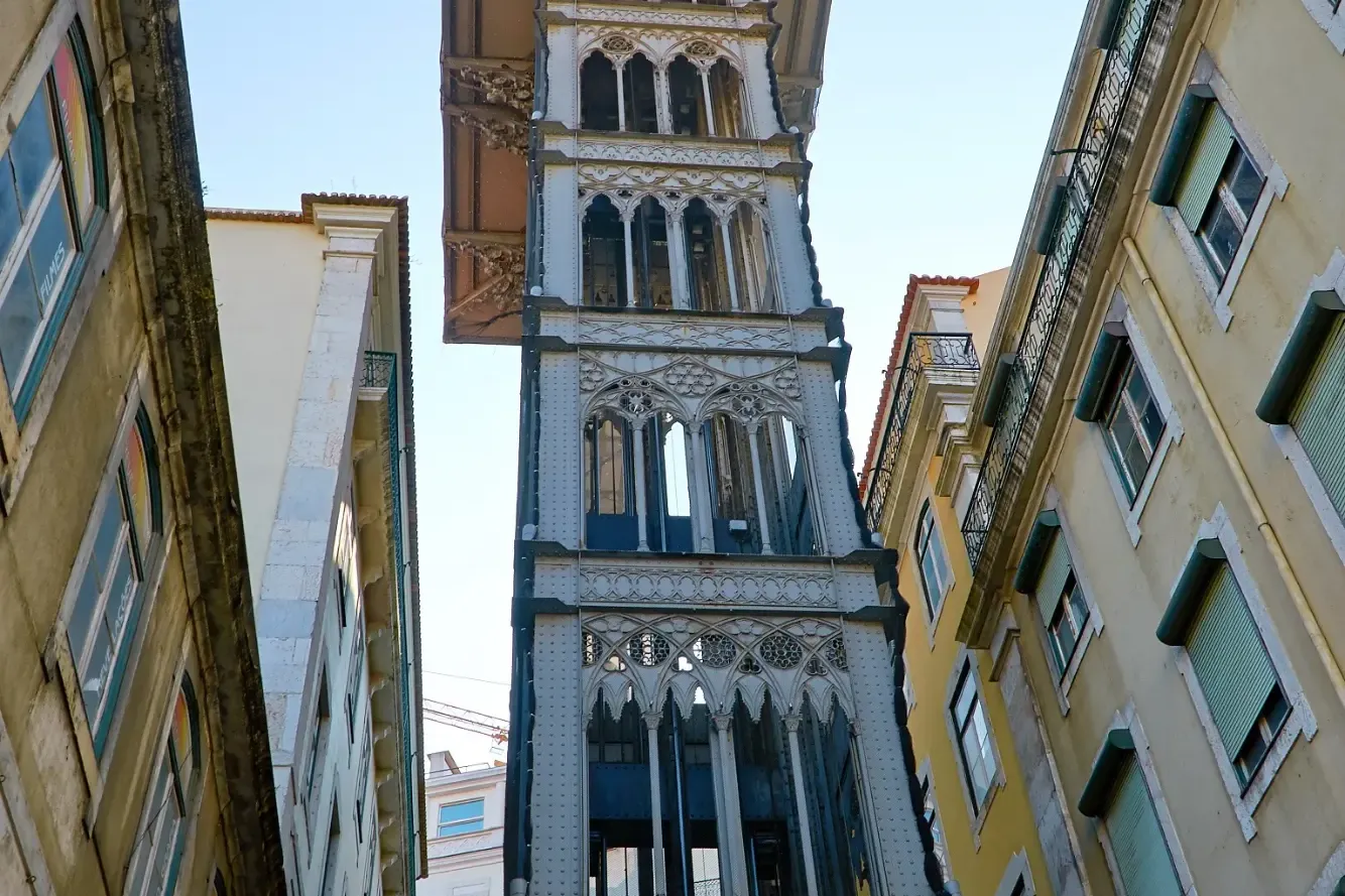The neo-Gothic Santa Justa Lift, an iron elevator in Lisbon, viewed from street level between buildings.