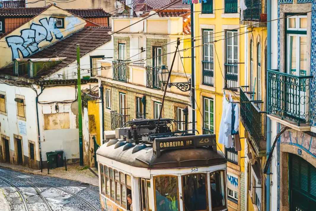 Yellow Tram 28 climbing a steep, cobbled street lined with traditional tiled buildings in Lisbon.