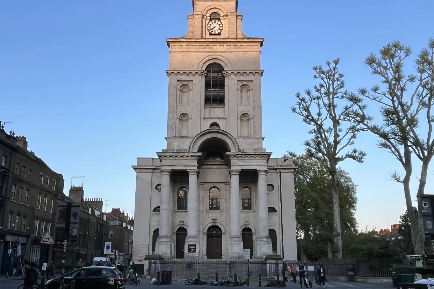 Christ Church Spitalfields seen from a cobbled street corner, its stone facade and steeple lit by the setting sun.