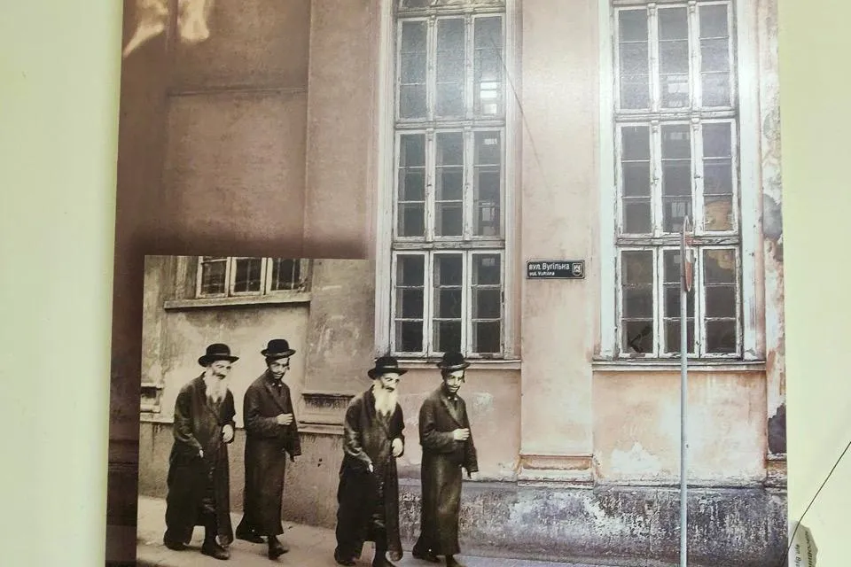 Poster on a wall showing a collage of a historical black-and-white photo of four Jewish men walking on a cobbled street, o...