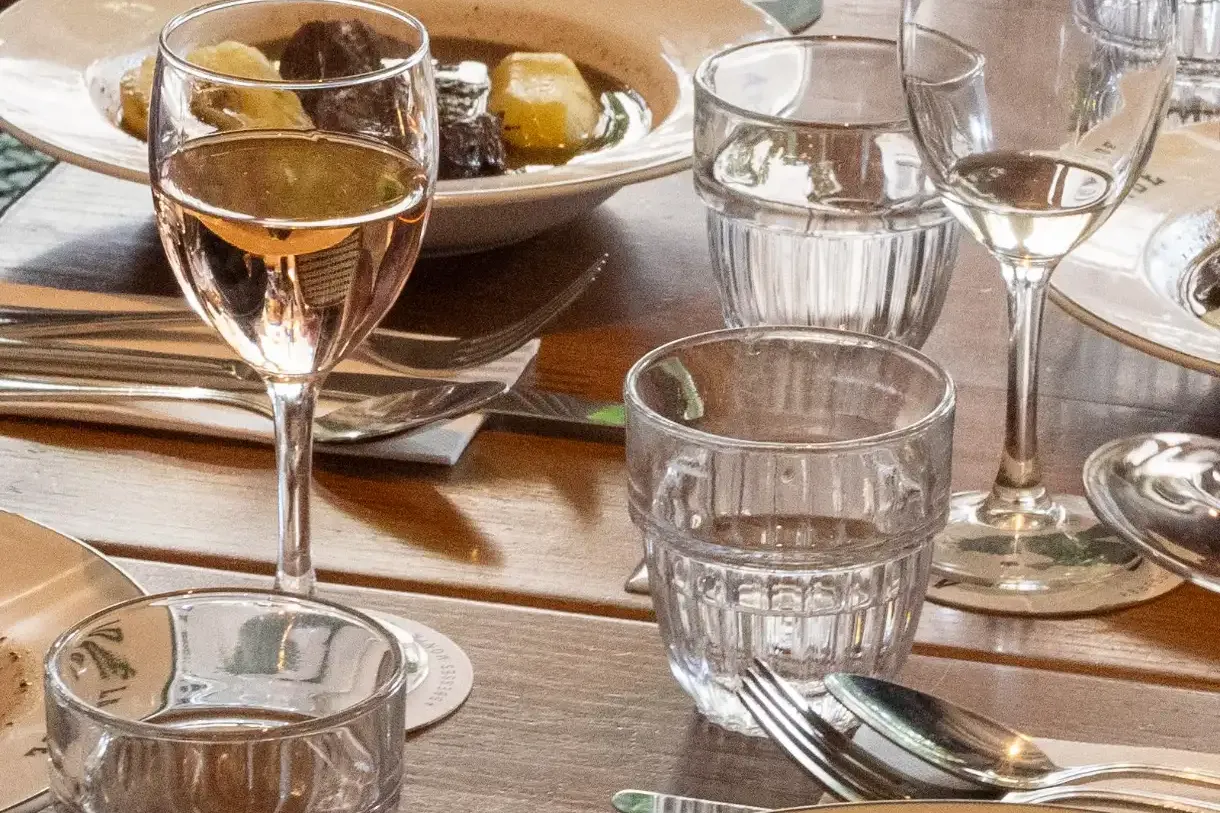 A dining table set with plates of stew, one reading 'ADÉLAÏDE', glasses of water and rosé wine, and a bread basket.