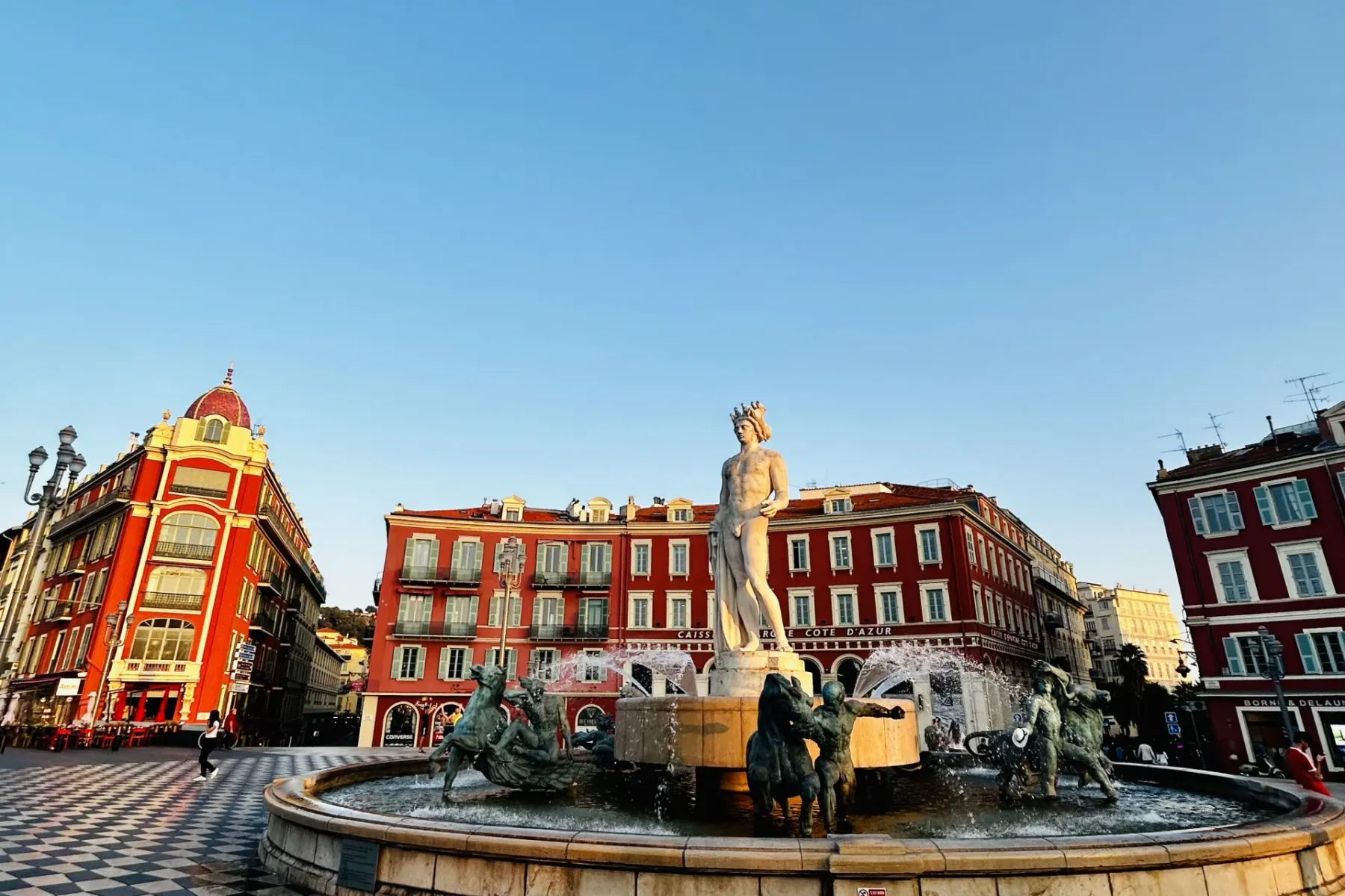 Fontaine du Soleil (Sun Fountain) in Nice, with the statue of Apollo and bronze figures, surrounded by red buildings under...