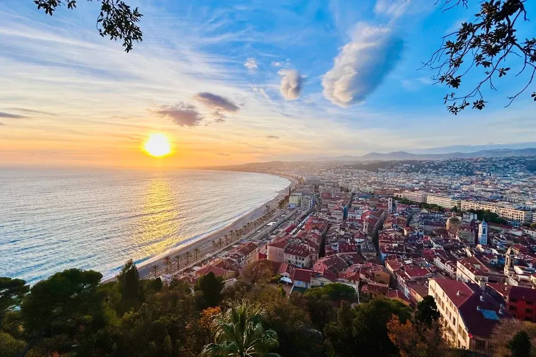 Aerial view of Nice coastline at sunset, with the Promenade des Anglais, Mediterranean Sea, and city buildings under an or...
