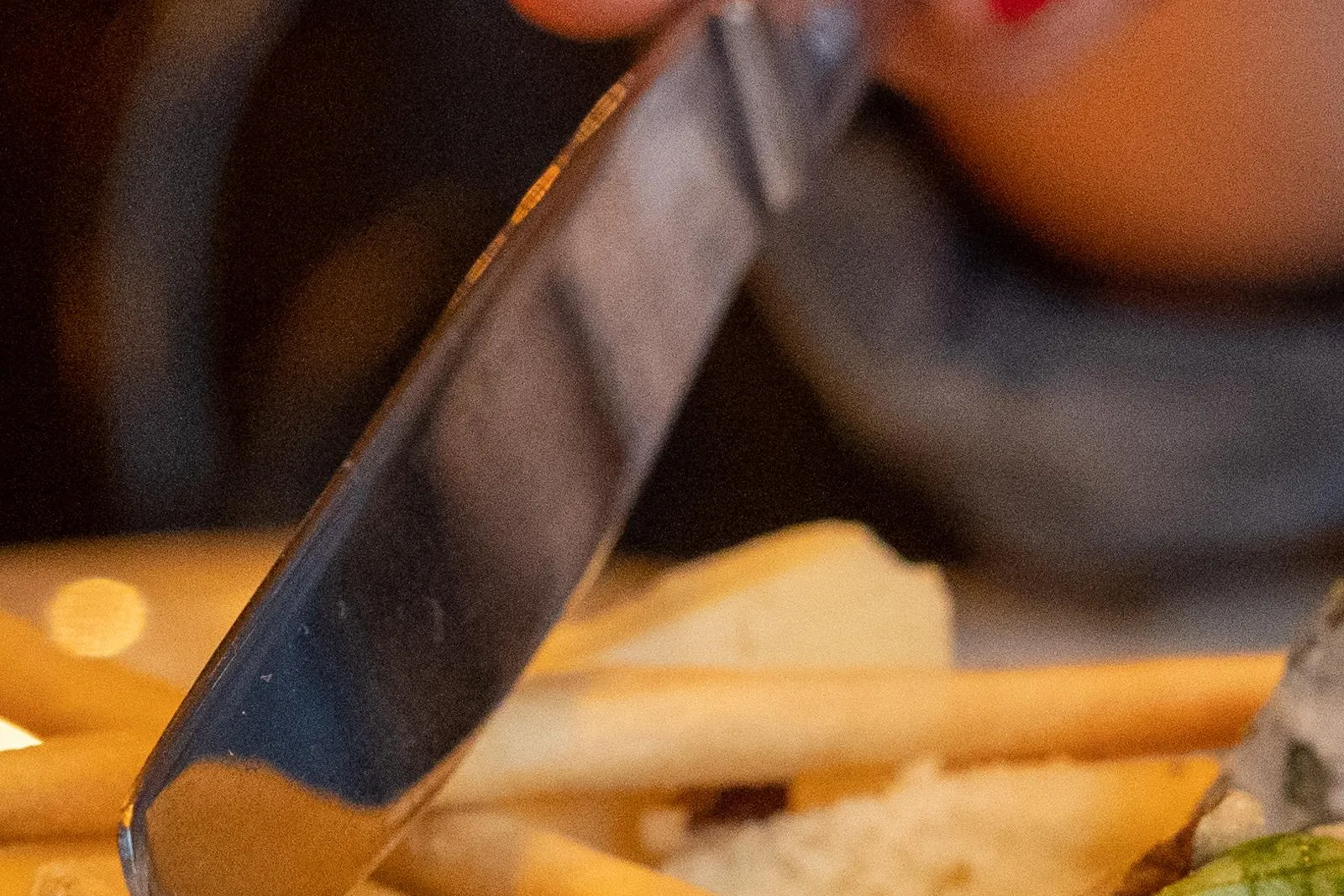 Close-up of a hand with red nail polish cutting a slice of white-rinded cheese on a plate with breadsticks.