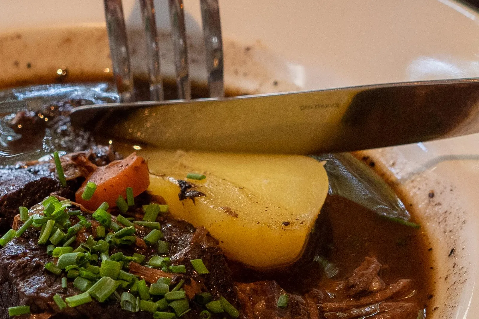 Close-up of a French stew with potato and fresh chives, a fork and knife cutting into it.