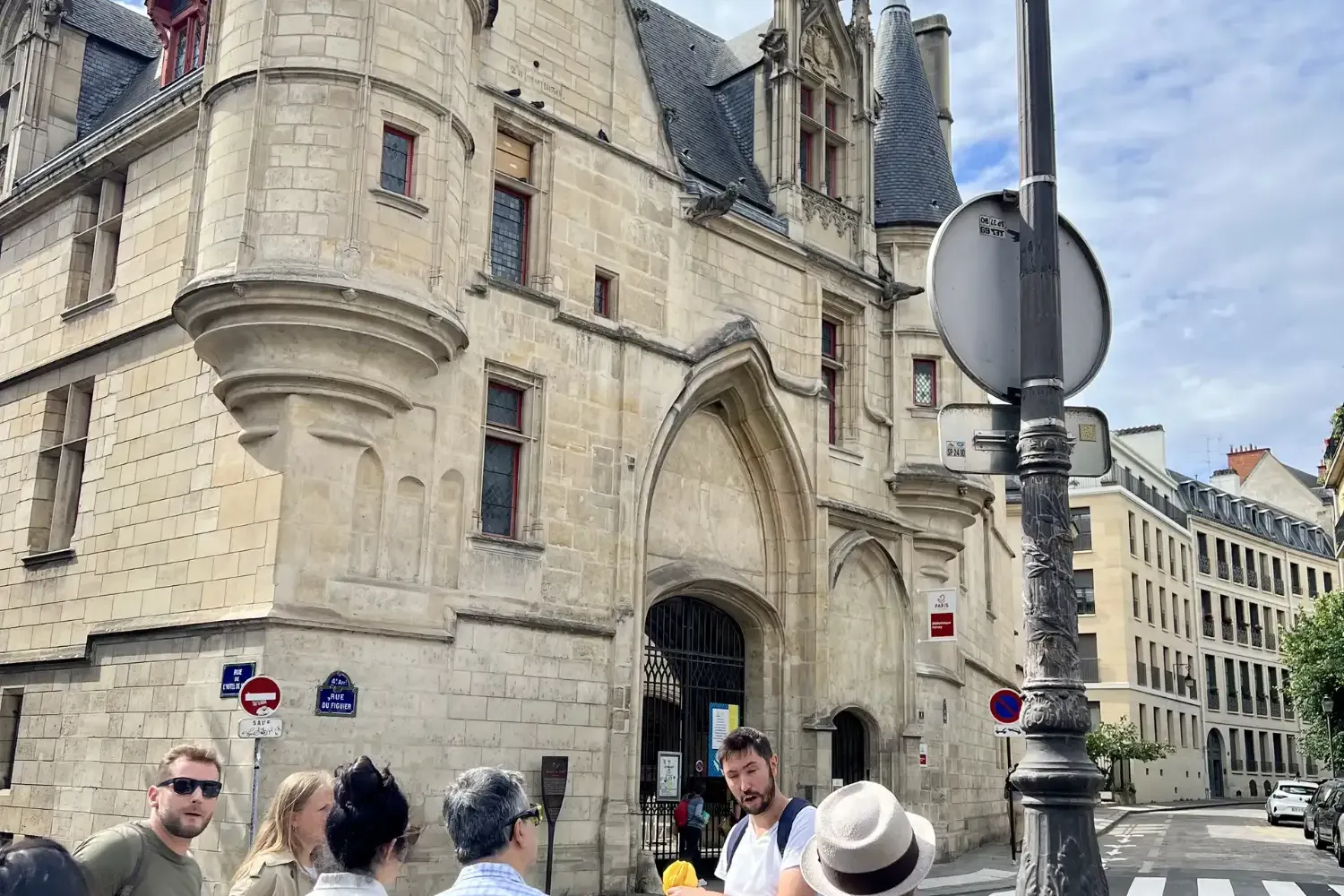 Tour guide addressing a small group of tourists in front of the historic Hôtel de Sens building in Paris on a cloudy day.