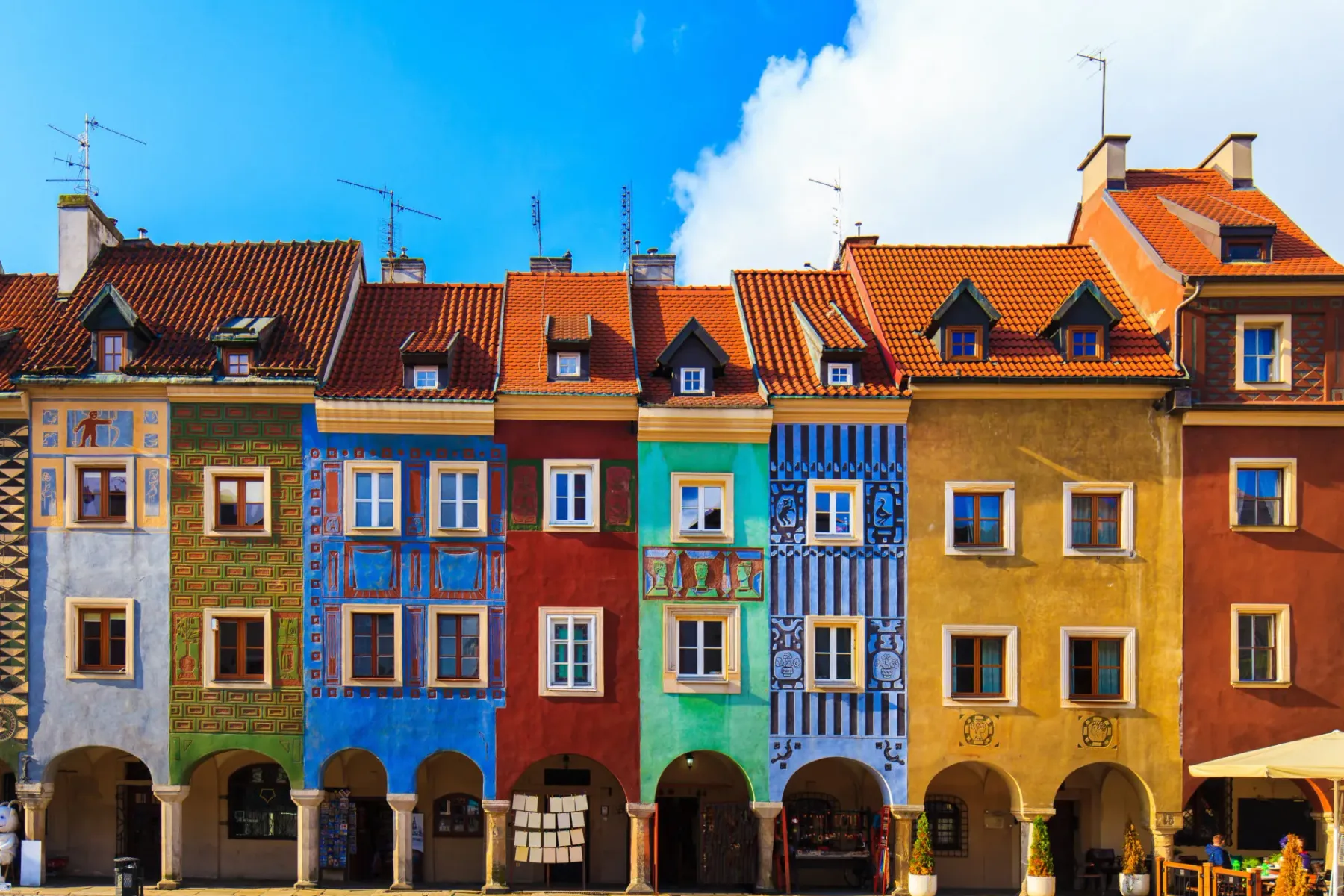 Row of colorful historic houses with tiled roofs and arched ground floors on a cobblestone square in Poznan.