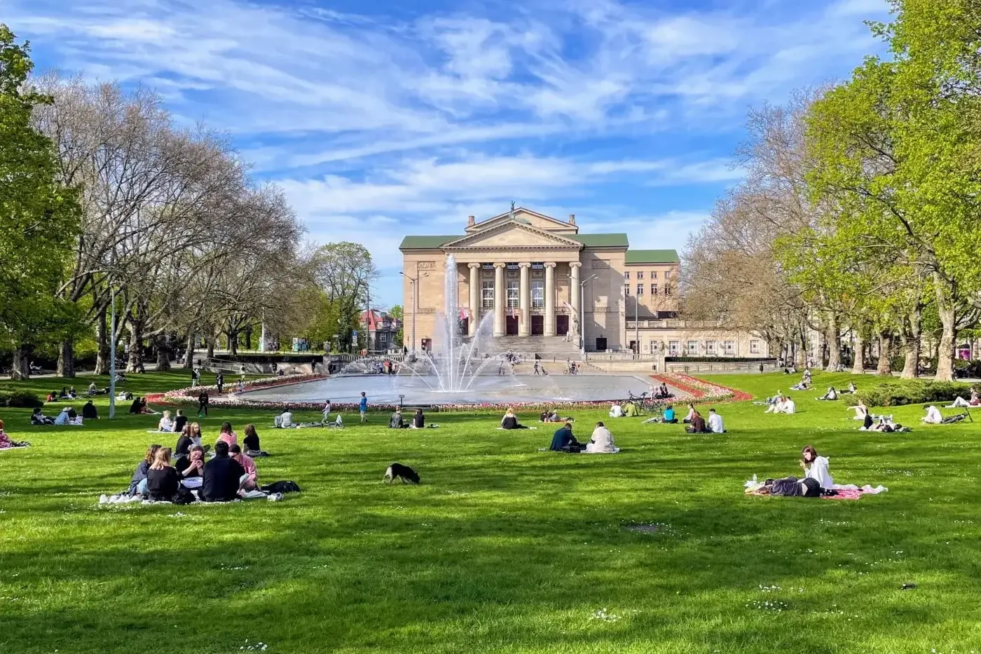 Gebäude des Großen Theaters, Springbrunnen und Menschen entspannen auf grünem Gras im Park in Posen an einem sonnigen Tag.