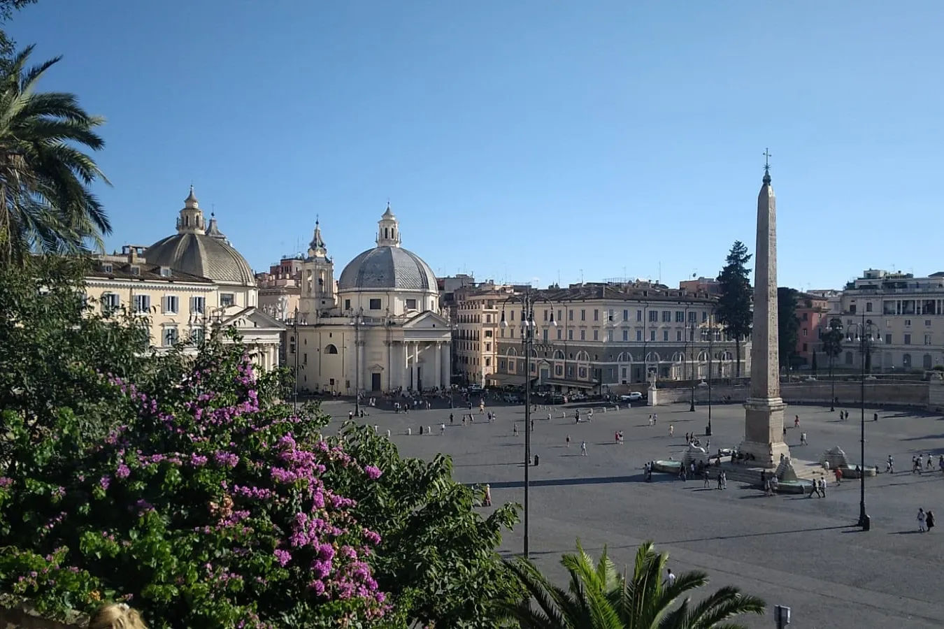 Elevated view of Piazza del Popolo in Rome showing the Flaminio Obelisk, twin churches, and people walking in the square.
