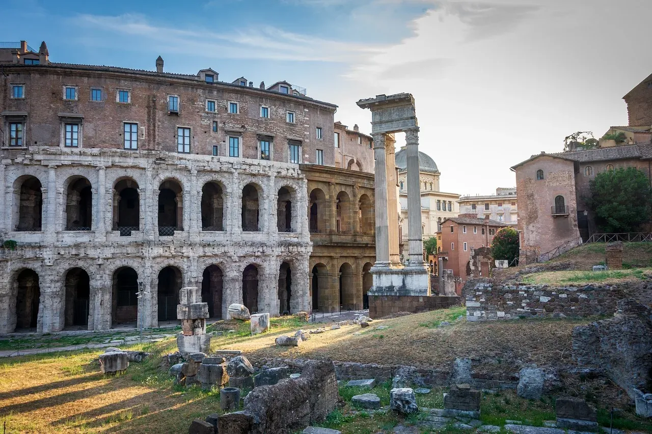 Ancient Theatre of Marcellus ruins with arched facade, modern buildings above, and Roman columns and debris in foreground.