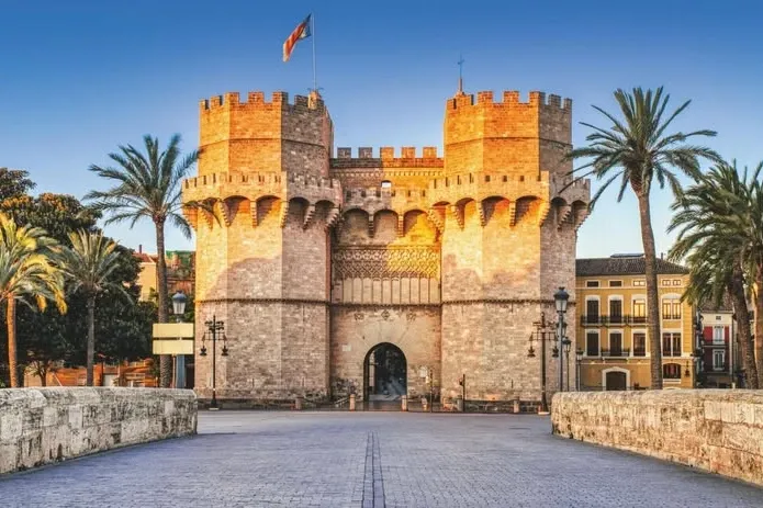 The Serranos Towers, a historic city gate in Valencia, viewed from a bridge at sunrise.
