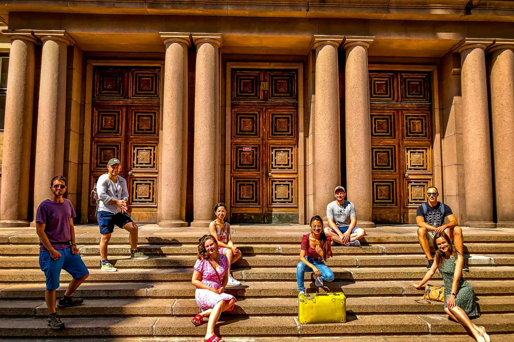 Happy tourists pose on the steps of a beautiful building in Helsinki.