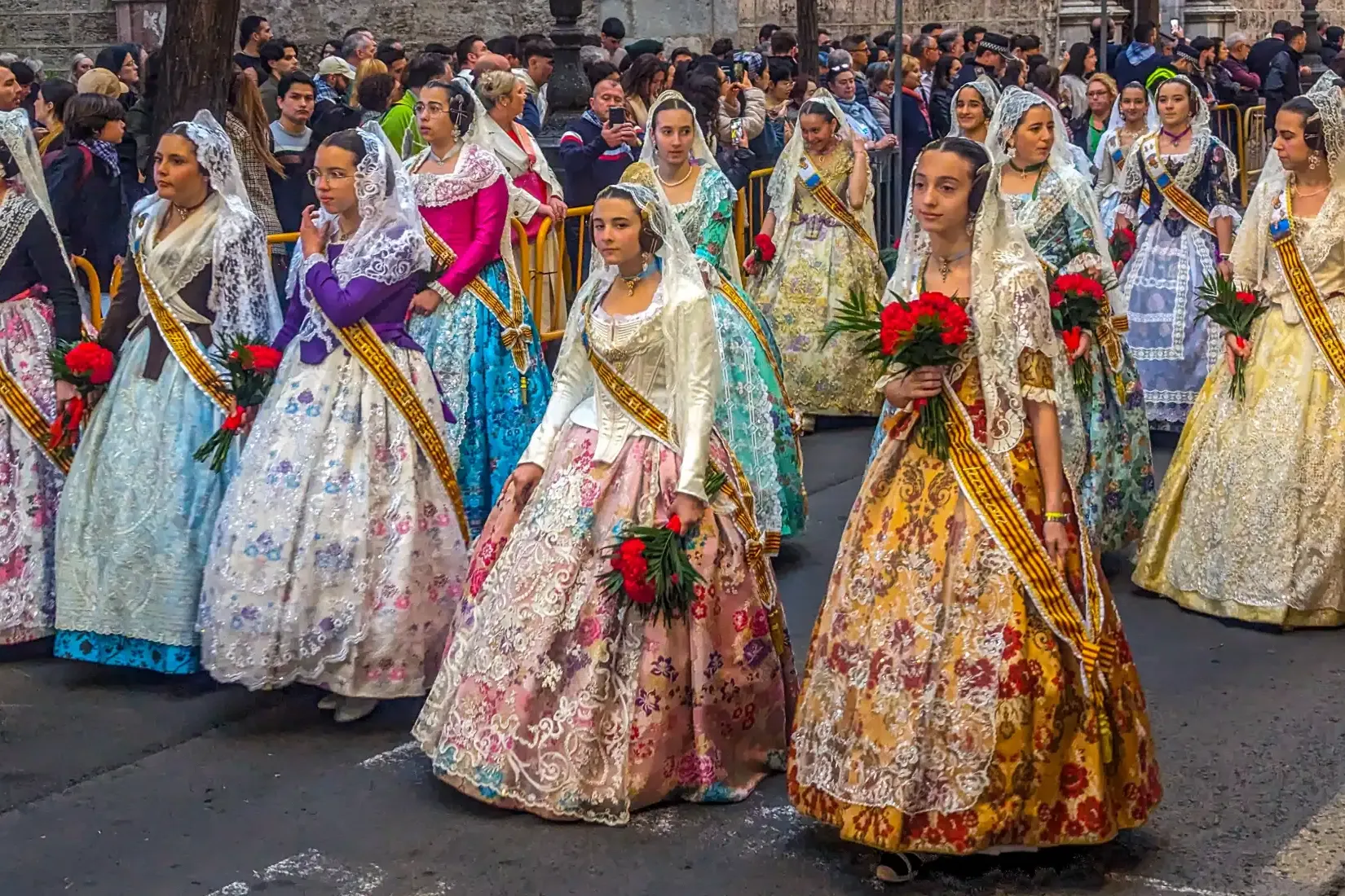 A group of women and girls in colourful, traditional Fallera dresses during a street parade in Valencia.