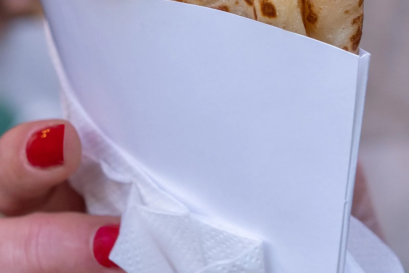 Close-up of a person's hand with red nail polish holding a folded crepe in a white paper holder.