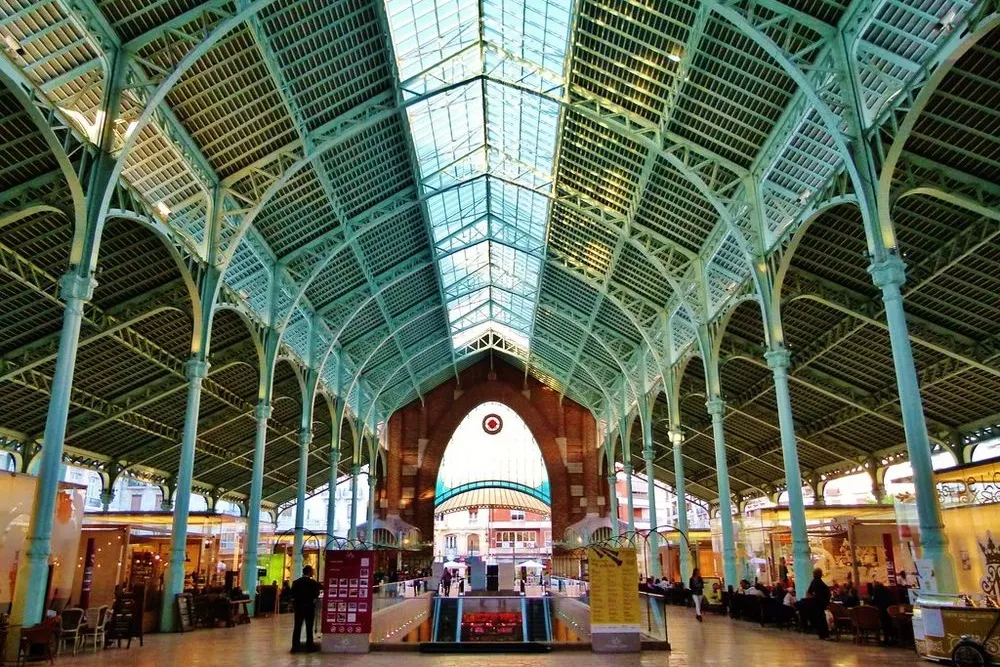 High vaulted ceiling with green metal trusses and a glass roof inside the Colón Market hall in Valencia.