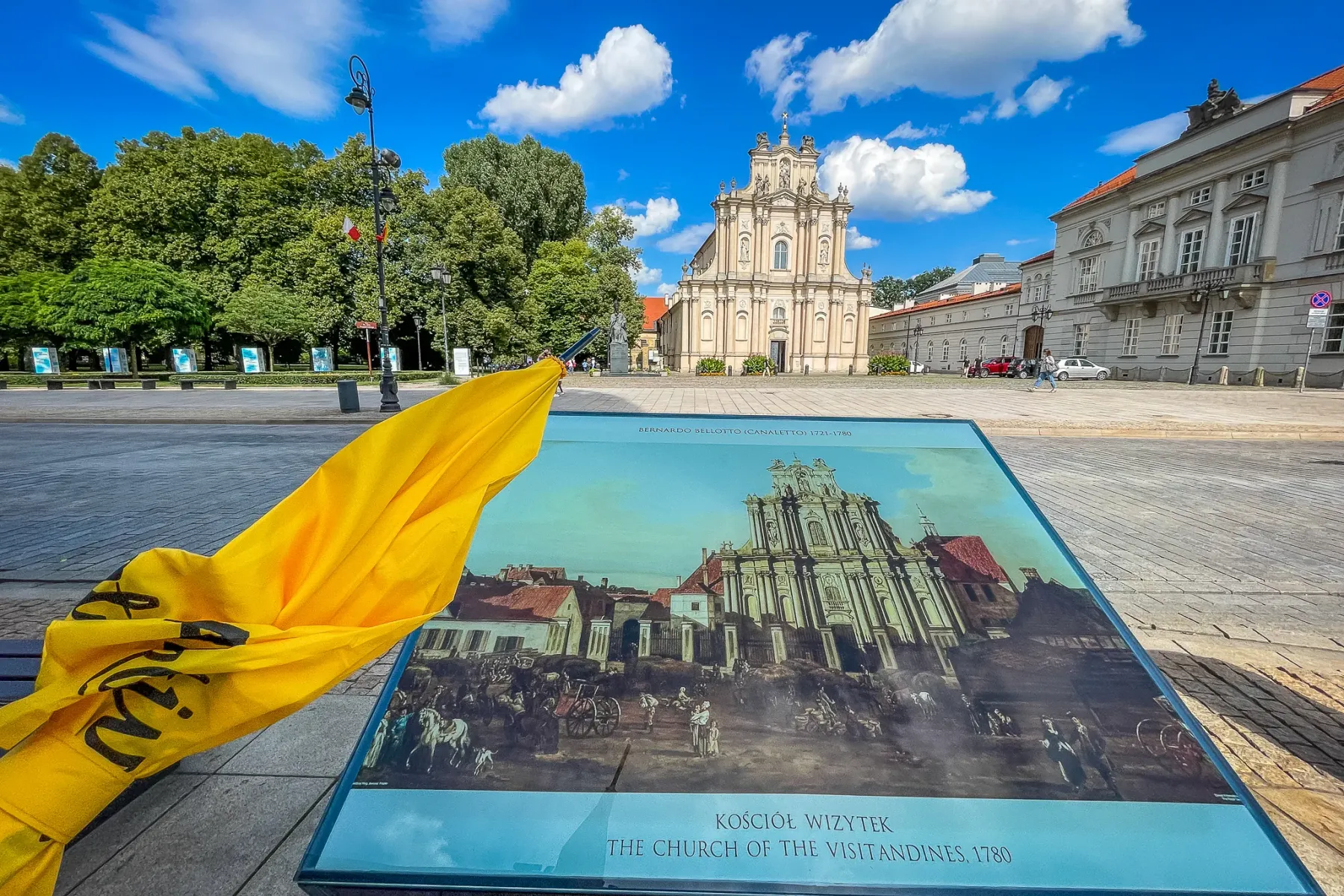 The Church of the Visitandines in Warsaw, a light-colored baroque building, seen behind a historical information board.