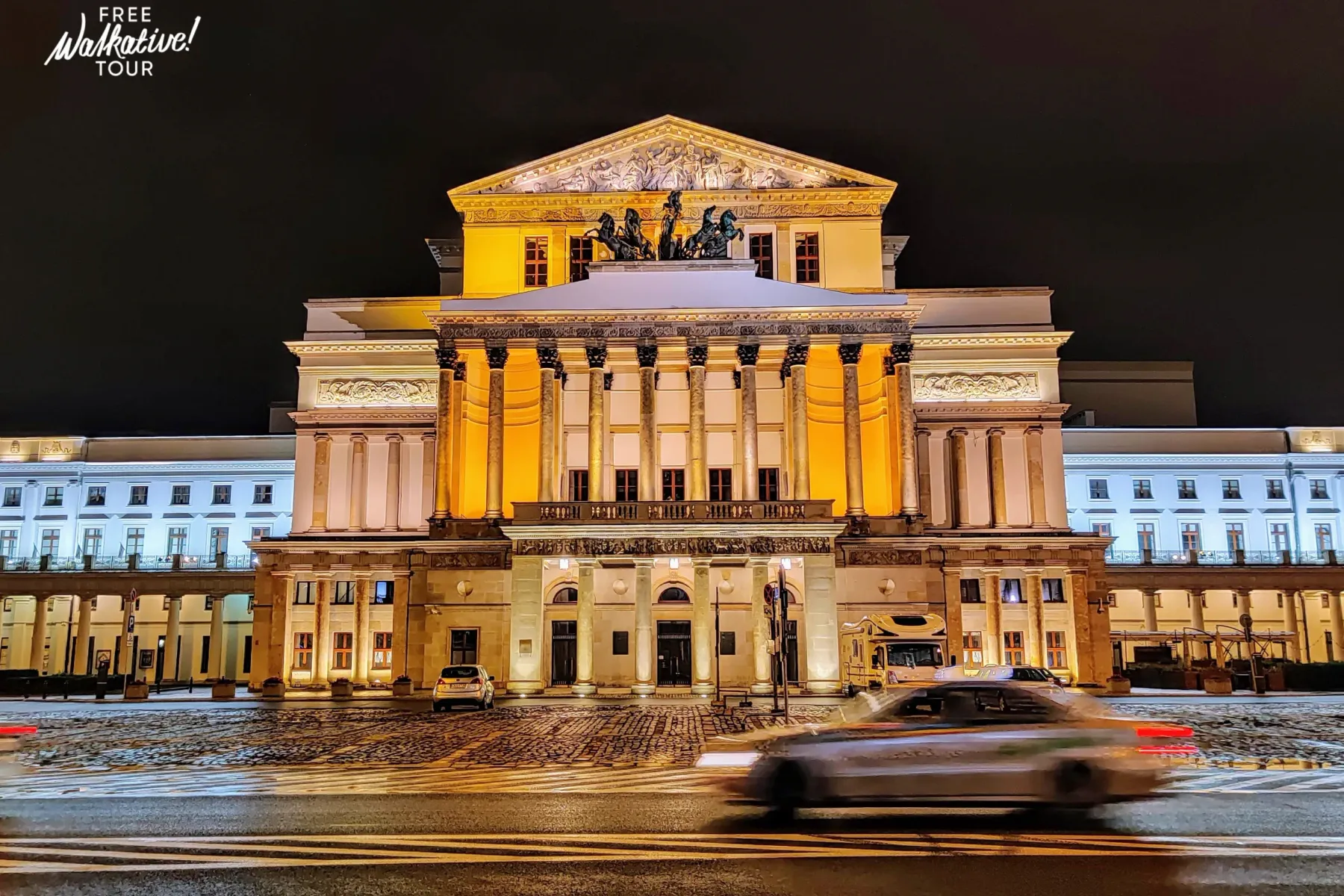 Grand Theatre in Warsaw at night, with a classical facade, columns, and sculptures, illuminated by warm lights. Snow on th...