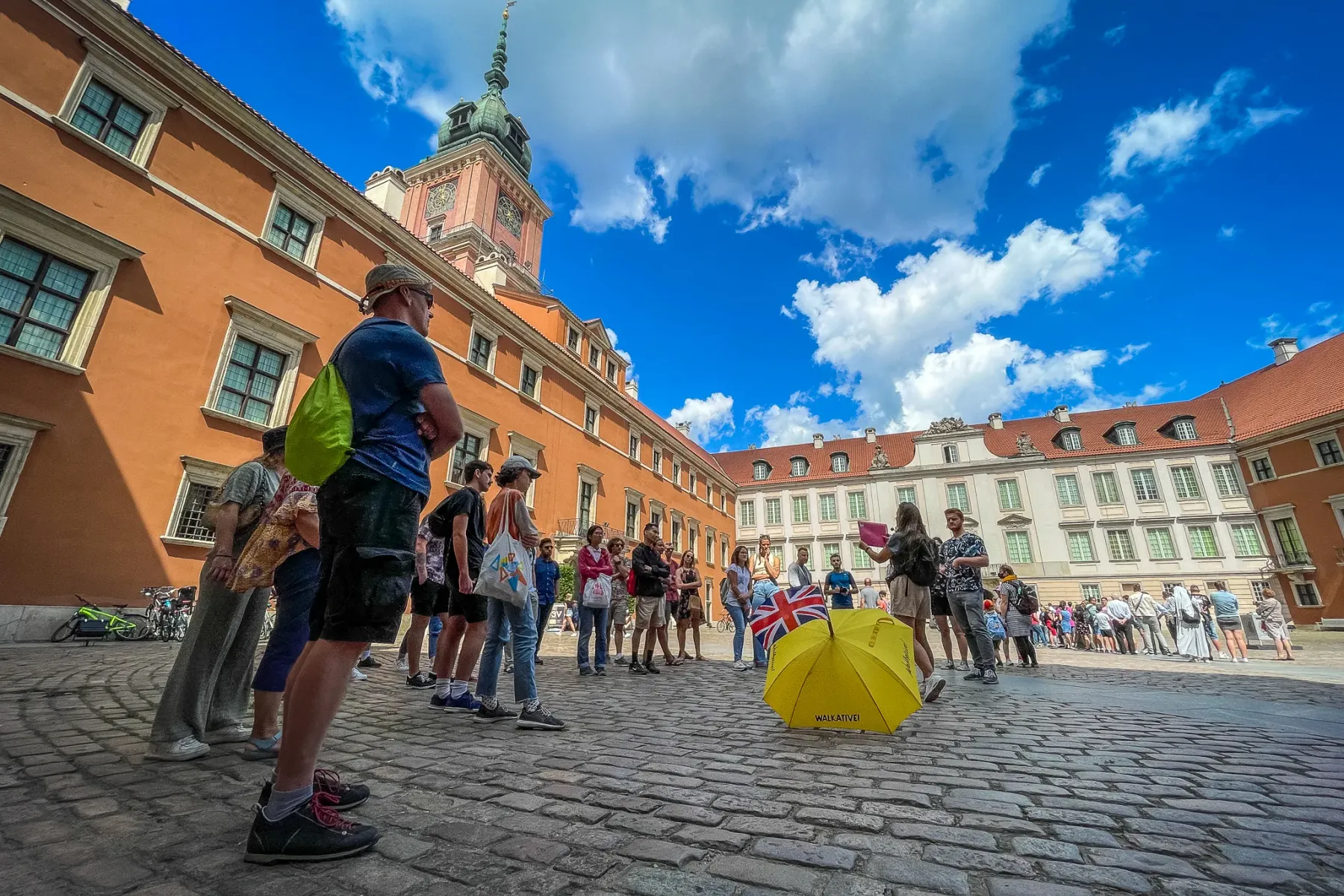 Tour group with guide and yellow umbrella on a cobblestone courtyard in front of Warsaw Royal Castle.