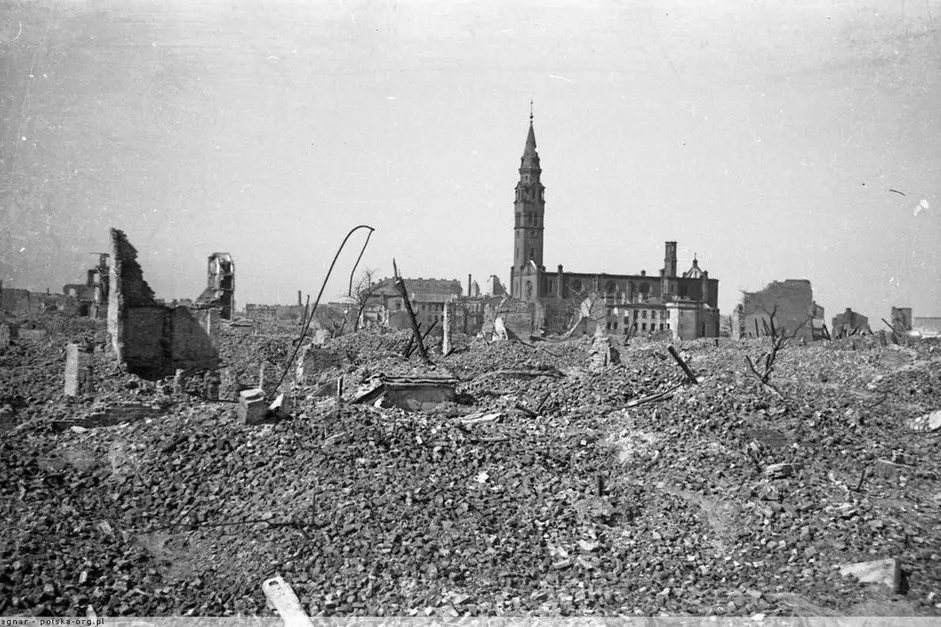 Black and white photo of a city devastated by war, showing a vast field of rubble in the foreground and a damaged church w...