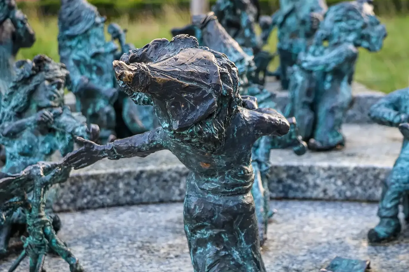 Group of bronze dwarf sculptures with green patina in Wroclaw. One dwarf in foreground extends its arm towards another on ...