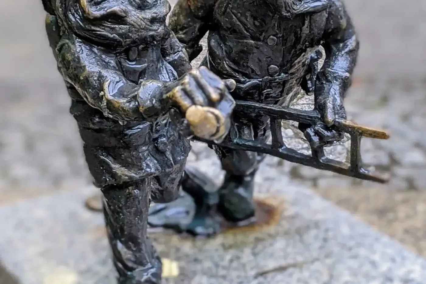 Two dark bronze dwarf statues with golden helmets, one bearded holding a pickaxe, the other with a ladder, on a granite pl...