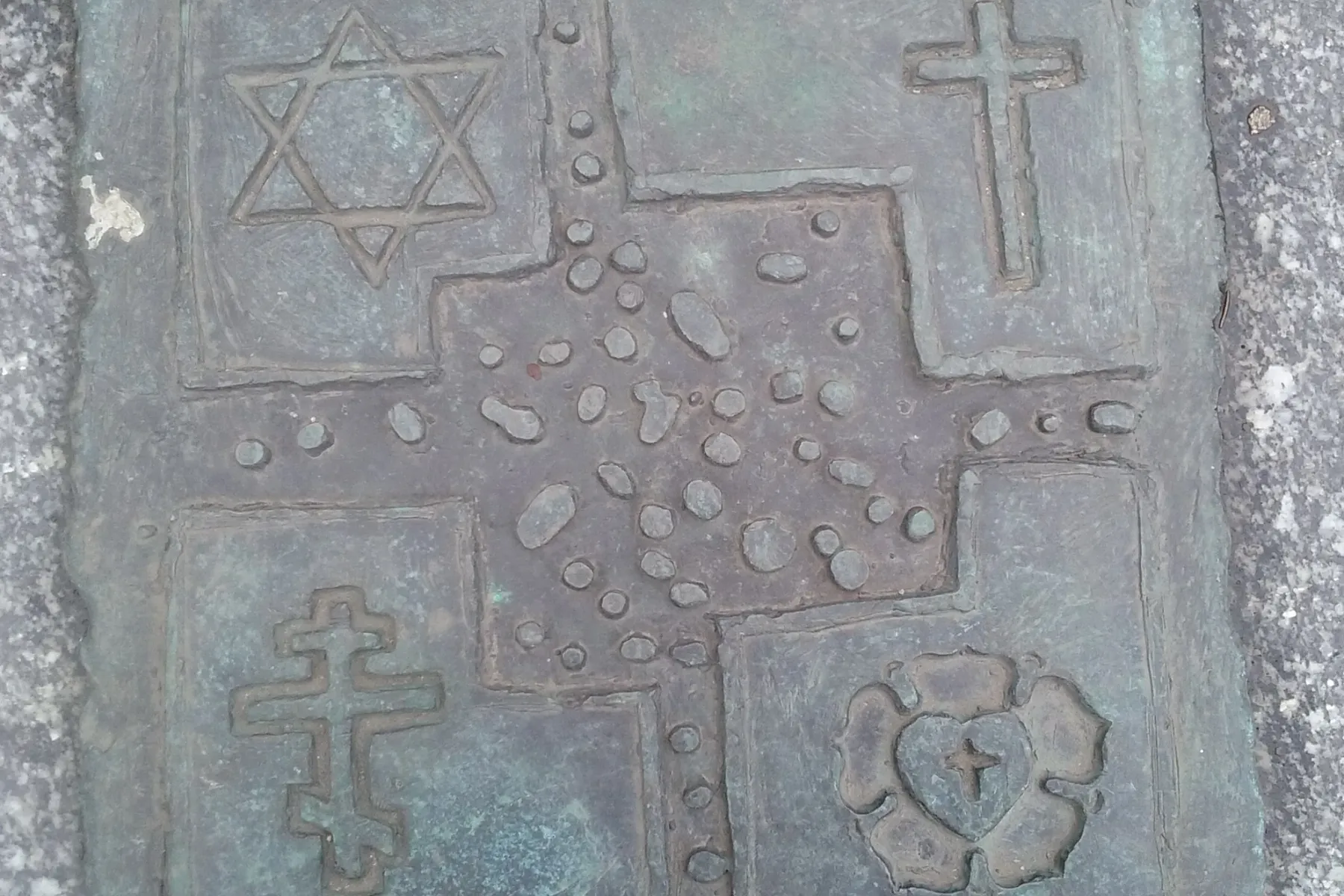Bronze plaque with four religious symbols: Star of David, Latin cross, Orthodox cross, and Luther rose, embedded in granite.