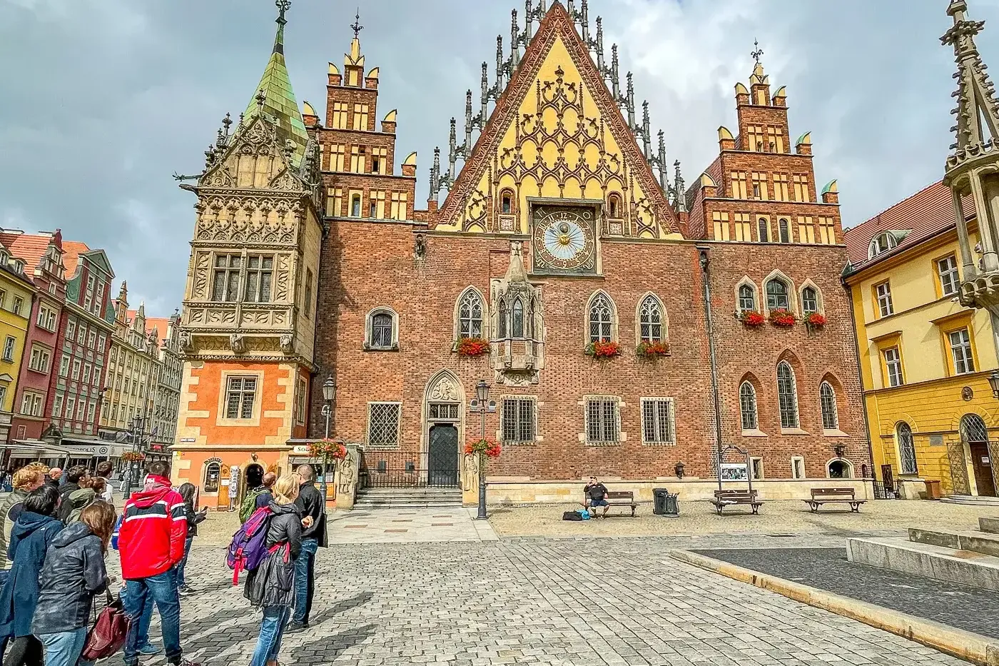 Wroclaw Old Town Hall, a large brick gothic building with a tall clock tower, stands on a cobblestone market square with a...