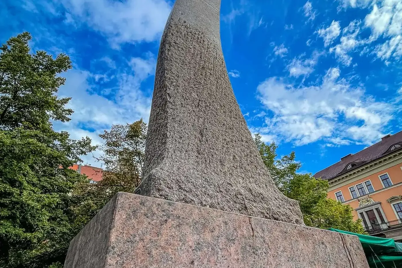 Tall, twisting abstract stone monument with a rough texture, on a granite base, against a bright blue sky with white clouds.