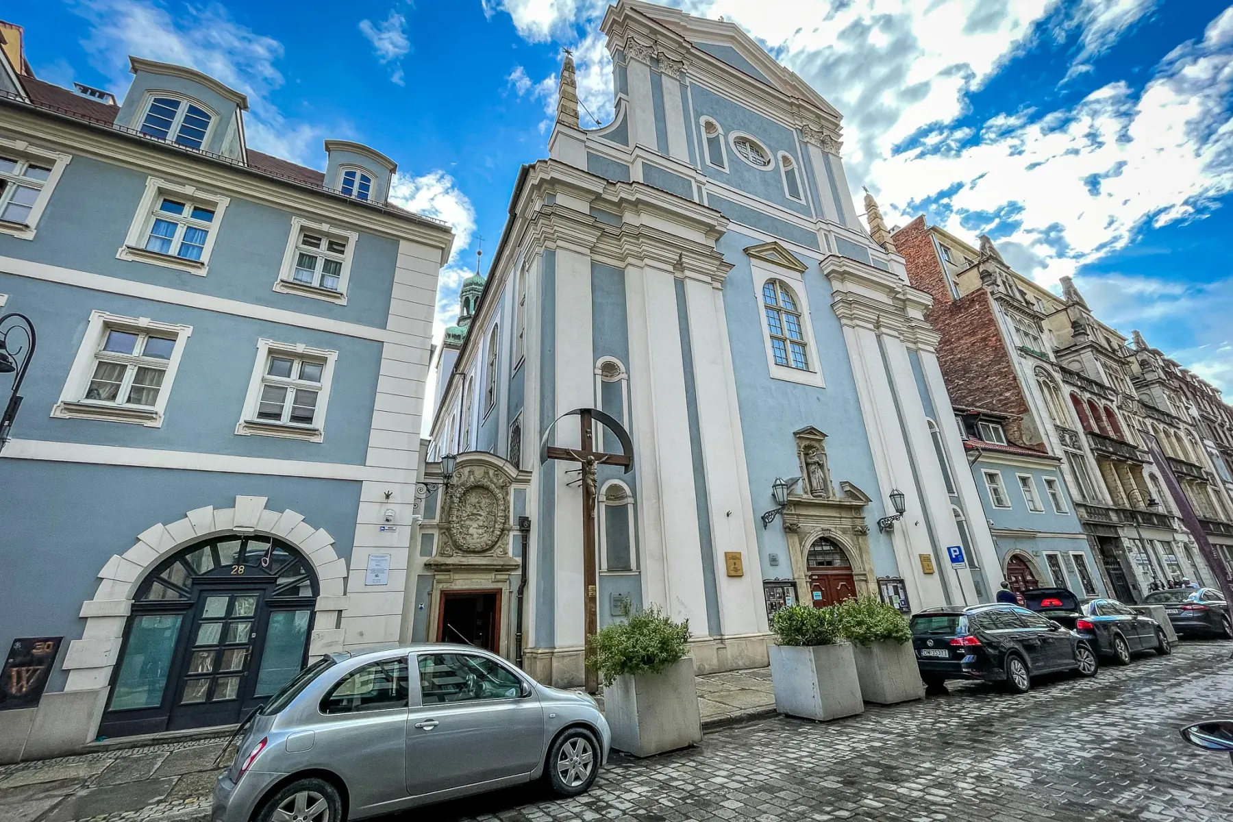 The light blue baroque facade of St. Anthony of Padua Church on a cobblestone street in Wrocław under a blue sky.